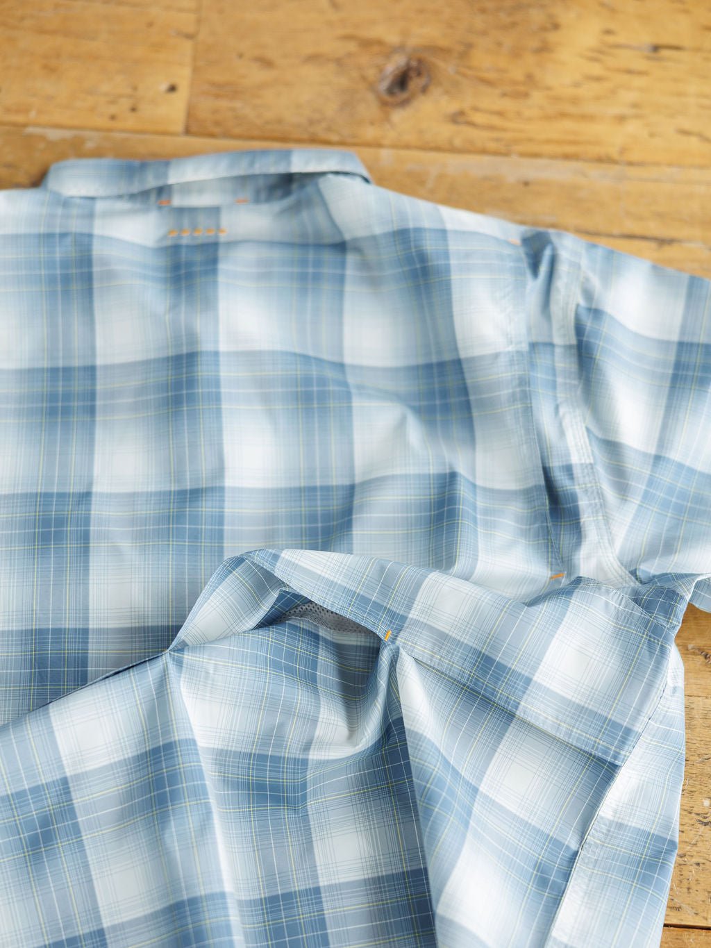 A Harrison Ariat Men's Blue Plaid Button Up from Savannah Sevens western life{&}style is laid out on a wooden surface, slightly rumpled, showing the back and part of a sleeve.