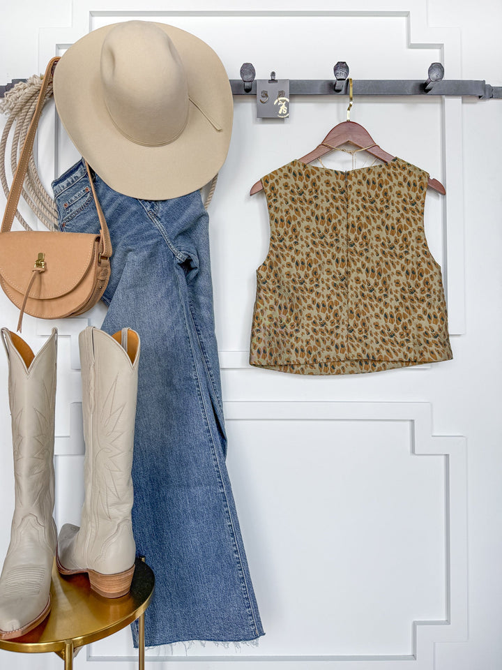 A beige hat, a tan purse, blue jeans, the Havana Textured Leopard Sleeveless Top by Savannah Sevens western life{&}style, and white cowboy boots are arranged neatly against a white wall with a decorative panel and coat hooks—perfect for young contemporary sizing.
