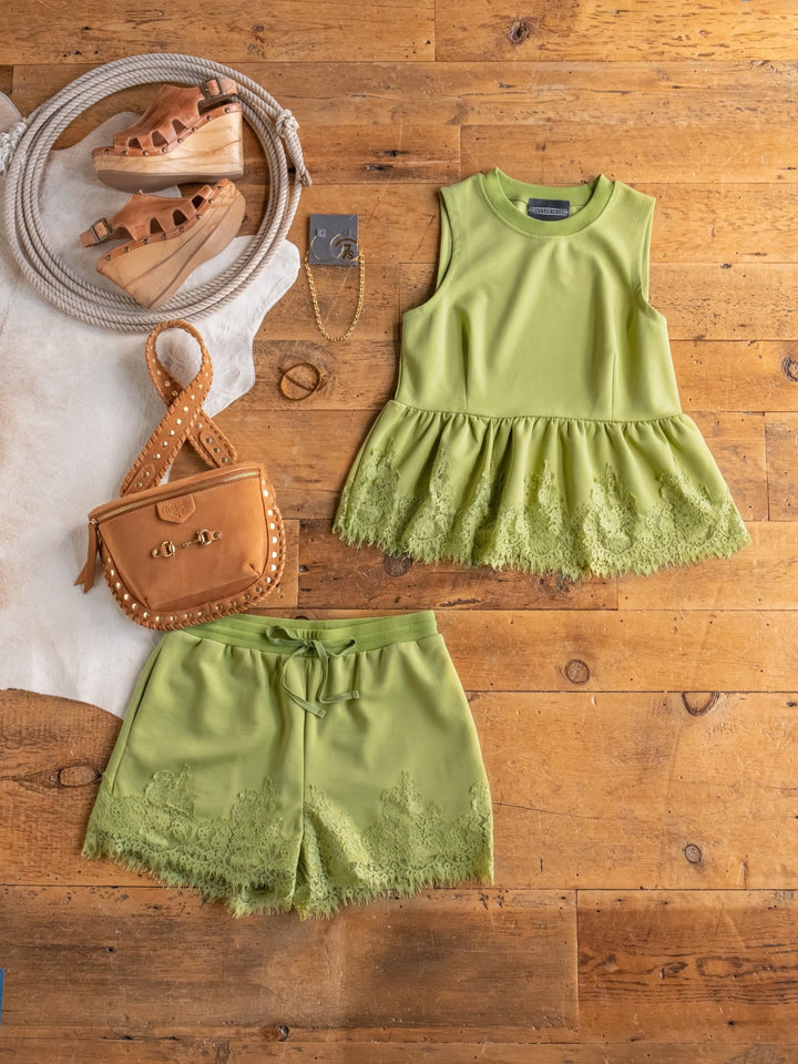 Flat lay of The Havasu {Set} from Savannah Sevens western life{&}style, featuring a citron sleeveless lace-hem top with matching high-waisted shorts, styled with a tan crossbody bag, wedge sandals, gold bracelet, and rope accessory on wood floor.