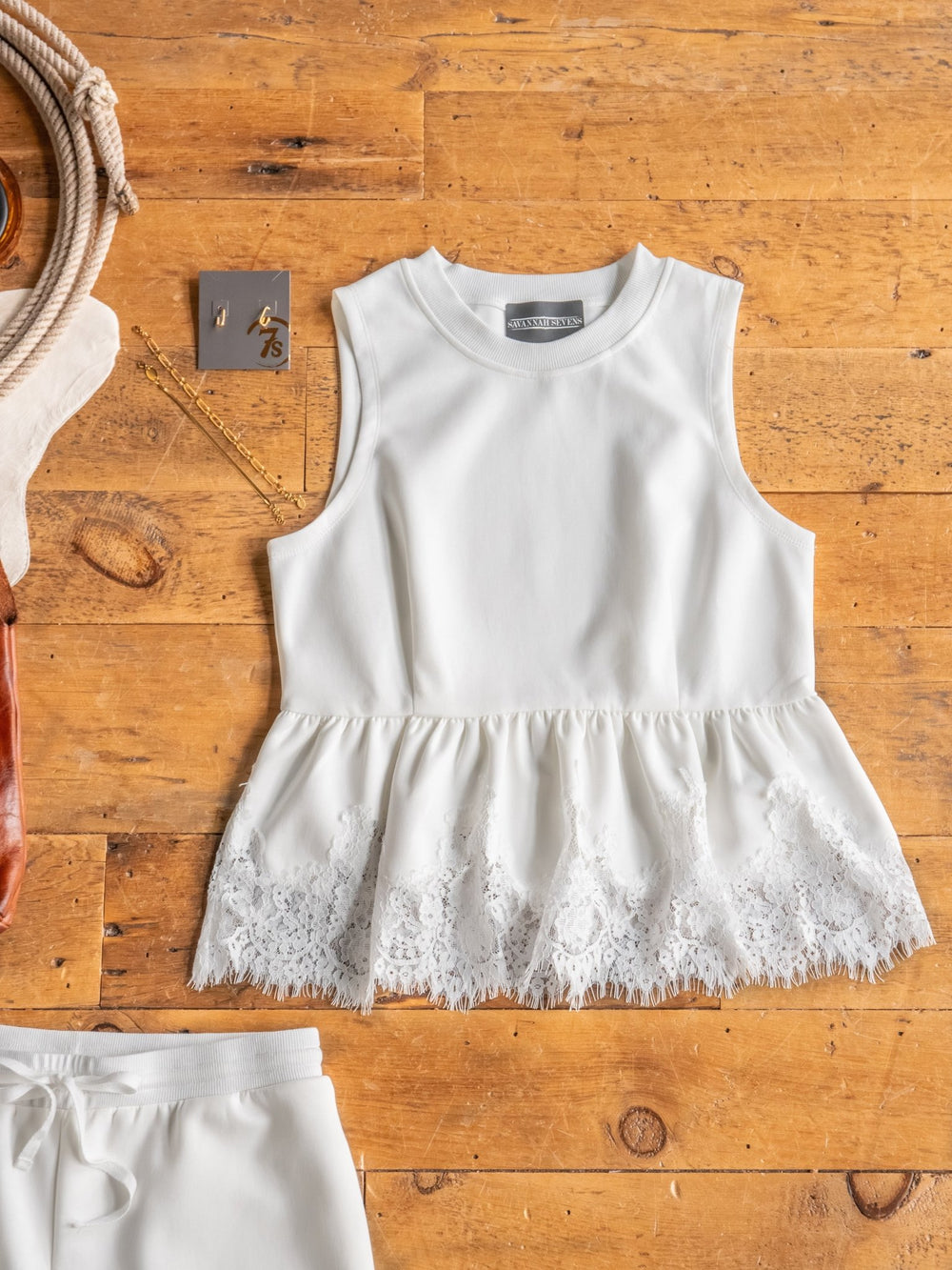 The Havasu Set by Savannah Sevens western life{&}style features a white sleeveless top with a lace scalloped hem, styled flat on wood and paired with gold jewelry and chic accessories.