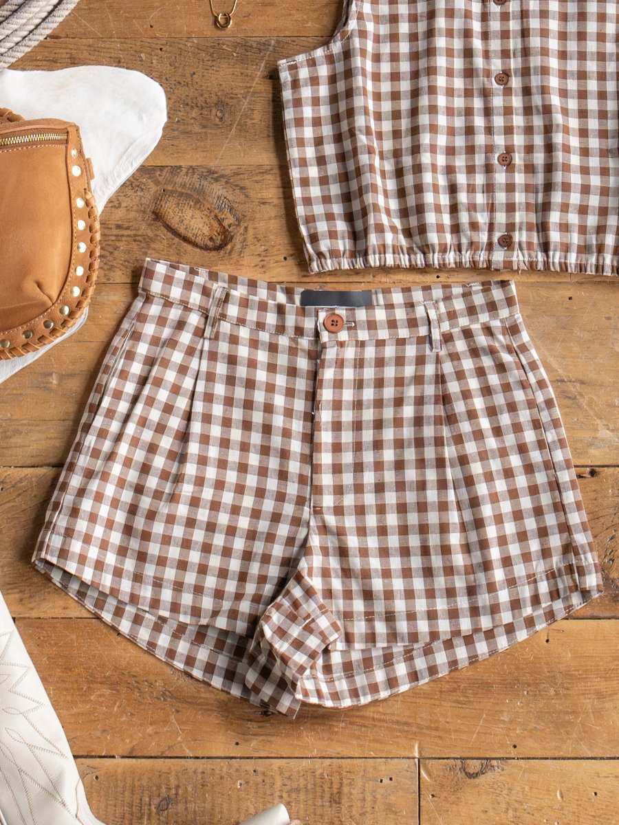 The Hazelton Chocolate Gingham Set by Savannah Sevens western life{&}style pairs brown and white pleated shorts with a matching sleeveless top and brown leather bag—an ideal women’s cotton summer outfit.