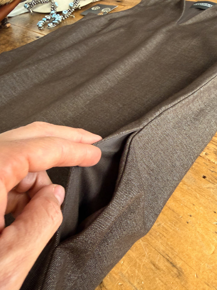 A hand reveals a hidden pocket in the Hazelwood Espresso Sleeveless Dress by Savannah Sevens western life{&}style, displayed flat on a wooden table with jewelry and earrings in the background.