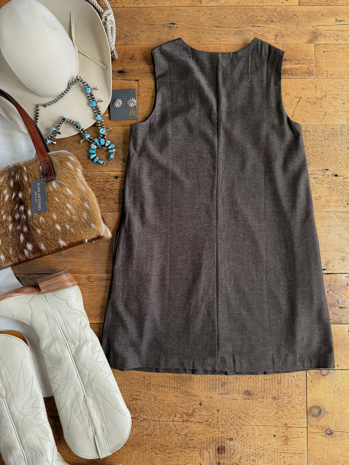 The Hazelwood Espresso Sleeveless Dress by Savannah Sevens western life{&}style is laid flat on a wooden floor, accompanied by white cowboy boots, a tan cowhide purse, a beige hat, blue jewelry, and a small black jewelry card.