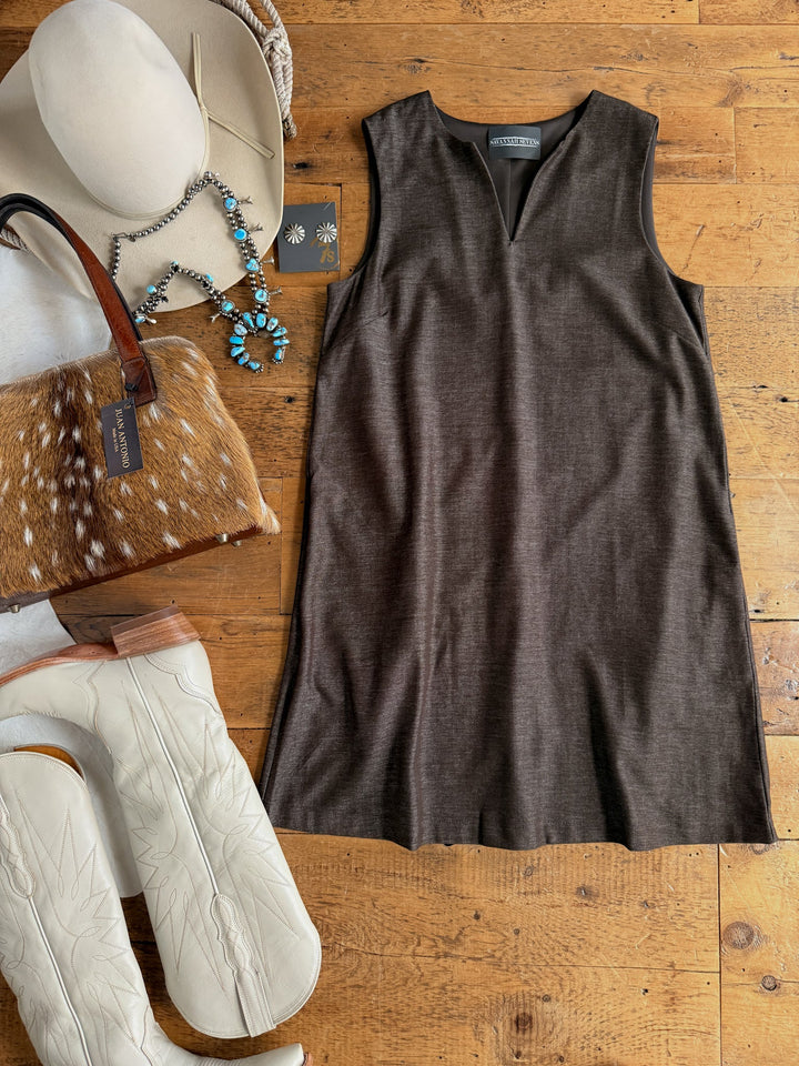 Flat lay of the Hazelwood Espresso Sleeveless Dress by Savannah Sevens western life{&}style, paired with cream cowboy boots, a fur bag, turquoise jewelry, earrings, a beige cowboy hat, and a necklace, all displayed on a wooden floor.