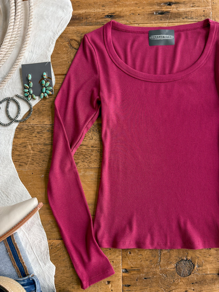 The Highland Brambleberry Ribbed Basic Top by Savannah Sevens western life{&}style is laid on a wooden surface beside turquoise earrings, a black hair tie, a straw hat, and jeans.