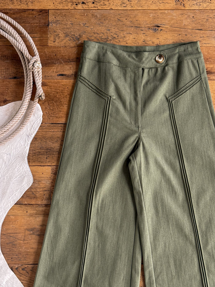 The Holt Olive Wide Leg Pants by Savannah Sevens western life{&}style, featuring a high waist and single-button waistband, are displayed on a wooden floor beside a coiled rope and a textured white cloth.