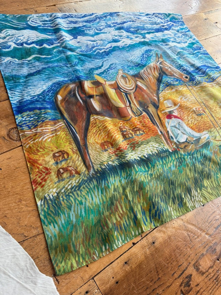 The Home On The Range Neck Scarf by Savannah Sevens western life{&}style features a Van Gogh-inspired scene of a cowboy resting next to his saddled brown horse in a grassy field under a swirling blue sky with yellow fields.