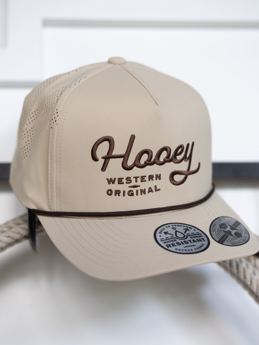 The Savannah Sevens western life{&}style Hooey Lansford Cap is a beige trucker hat with "Hooey Western Original" brown embroidery, an adjustable snapback, a rope detail above the brim, and two stickers on the flat bill.