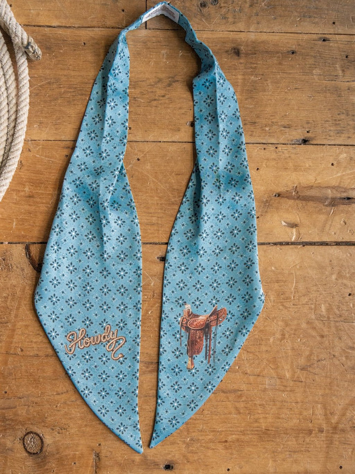 A Howdy Light Blue Satin Tie Scarf by Savannah Sevens western life{&}style, adorned with small black patterns and embroidered with "Howdy" and a saddle, is laid flat on a wooden surface beside a coiled rope.