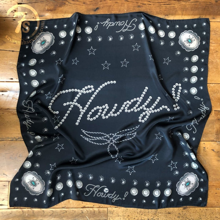 The Howdy Wild Rag {Noir} by Savannah Sevens western life{&}style is a black silk scarf featuring “Howdy!” in bold white dotted script with star and floral accents, shown with natural folds on a wooden floor.