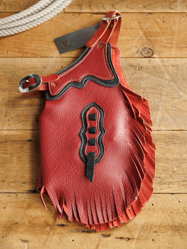 A red leather fringed spur strap with black accents and a silver buckle sits on wood, next to rope and a Savannah Sevens western life{&}style tag—perfect to pair with Hulett Chinks {Toddler & Youth} for any young cowkid's gear collection.