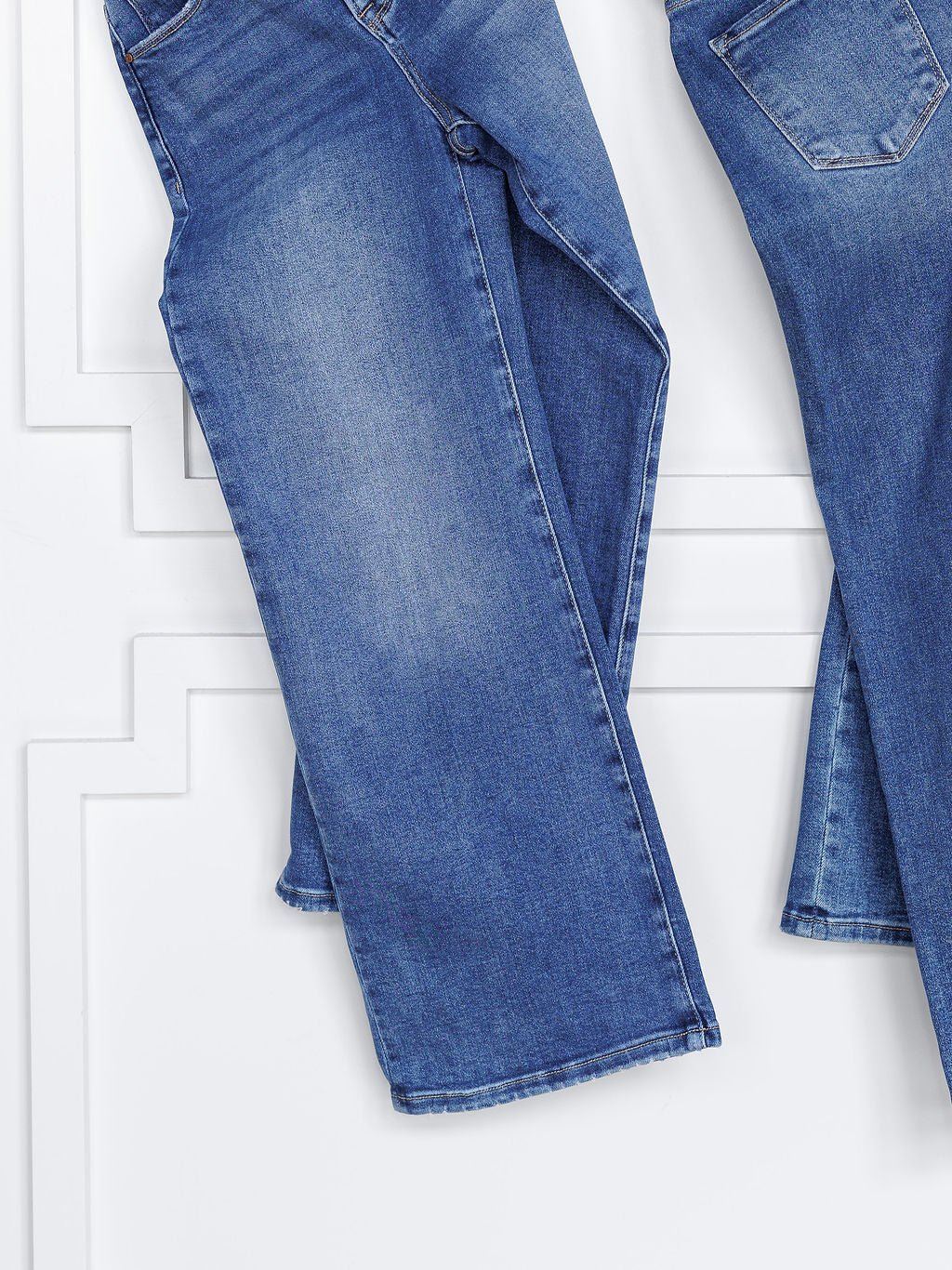 Two pairs of The Josey High Rise Wide Leg Crop Jeans by Savannah Sevens western life{&}style hang side by side against a white wall, displayed waist to hem to highlight their wide-leg crop style and tummy control feature.