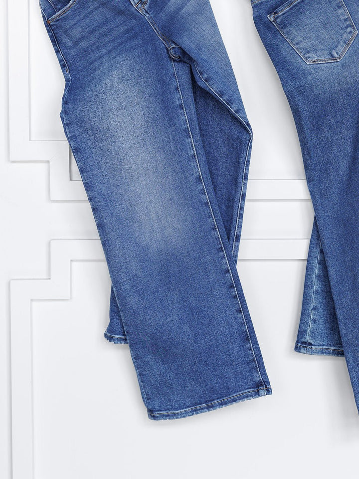 Two pairs of The Josey High Rise Wide Leg Crop Jeans by Savannah Sevens western life{&}style hang side by side against a white wall, displayed waist to hem to highlight their wide-leg crop style and tummy control feature.