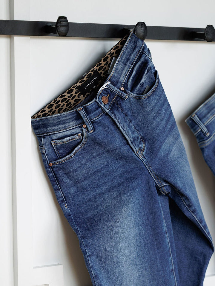 A pair of The Josey High Rise Wide Leg Crop Jean by Savannah Sevens western life{&}style hangs on a black hook, showcasing its blue wide leg crop design and a visible brown leopard print waistband lining.