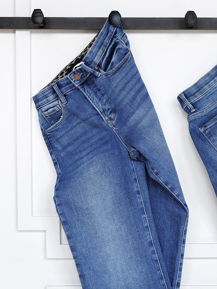 The Josey High Rise Wide Leg Crop Jean by Savannah Sevens western life{&}style in blue hangs by the belt loop from a black wall hook against a white paneled background.