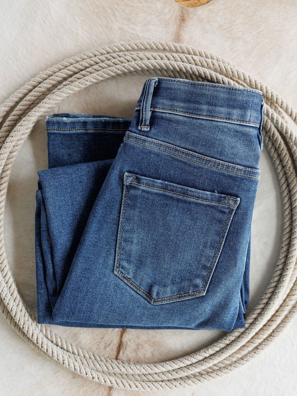 A pair of The Josey High Rise Wide Leg Crop Jeans by Savannah Sevens western life{&}style is folded inside a coiled rope on a light, textured surface.