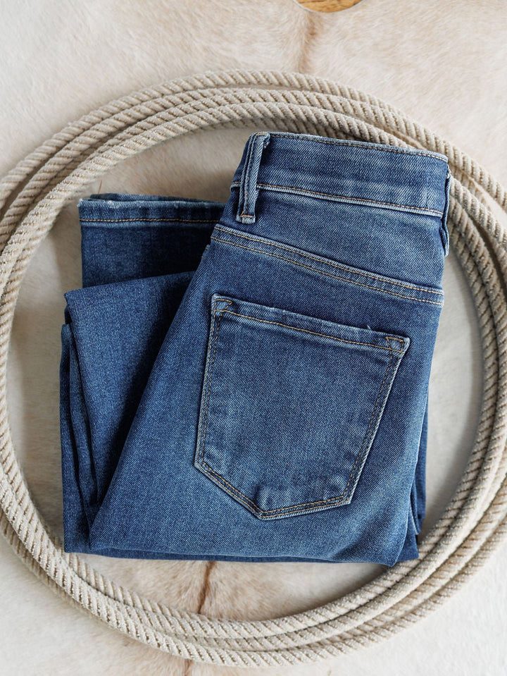 A pair of The Josey High Rise Wide Leg Crop Jeans by Savannah Sevens western life{&}style is folded inside a coiled rope on a light, textured surface.