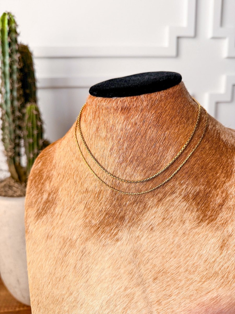 The Kahoka Necklace by Savannah Sevens western life{&}style, an 18K gold filled, hypoallergenic chain, is showcased on a brown and white cowhide jewelry bust with a potted cactus in the background against a white wall.