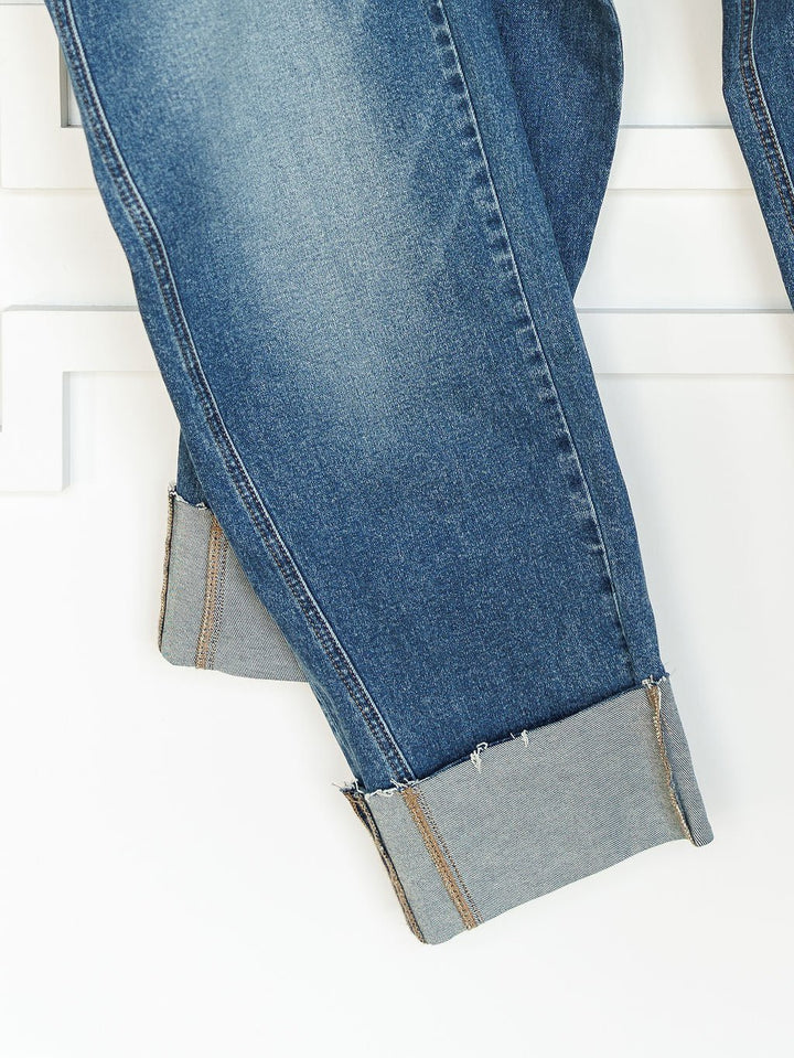 A close-up of The Kamden High Rise Barrel Jeans by Savannah Sevens western life{&}style, featuring medium wash denim, wide rolled cuffs with visible stitching, and subtle fading along the legs, set against a white background.