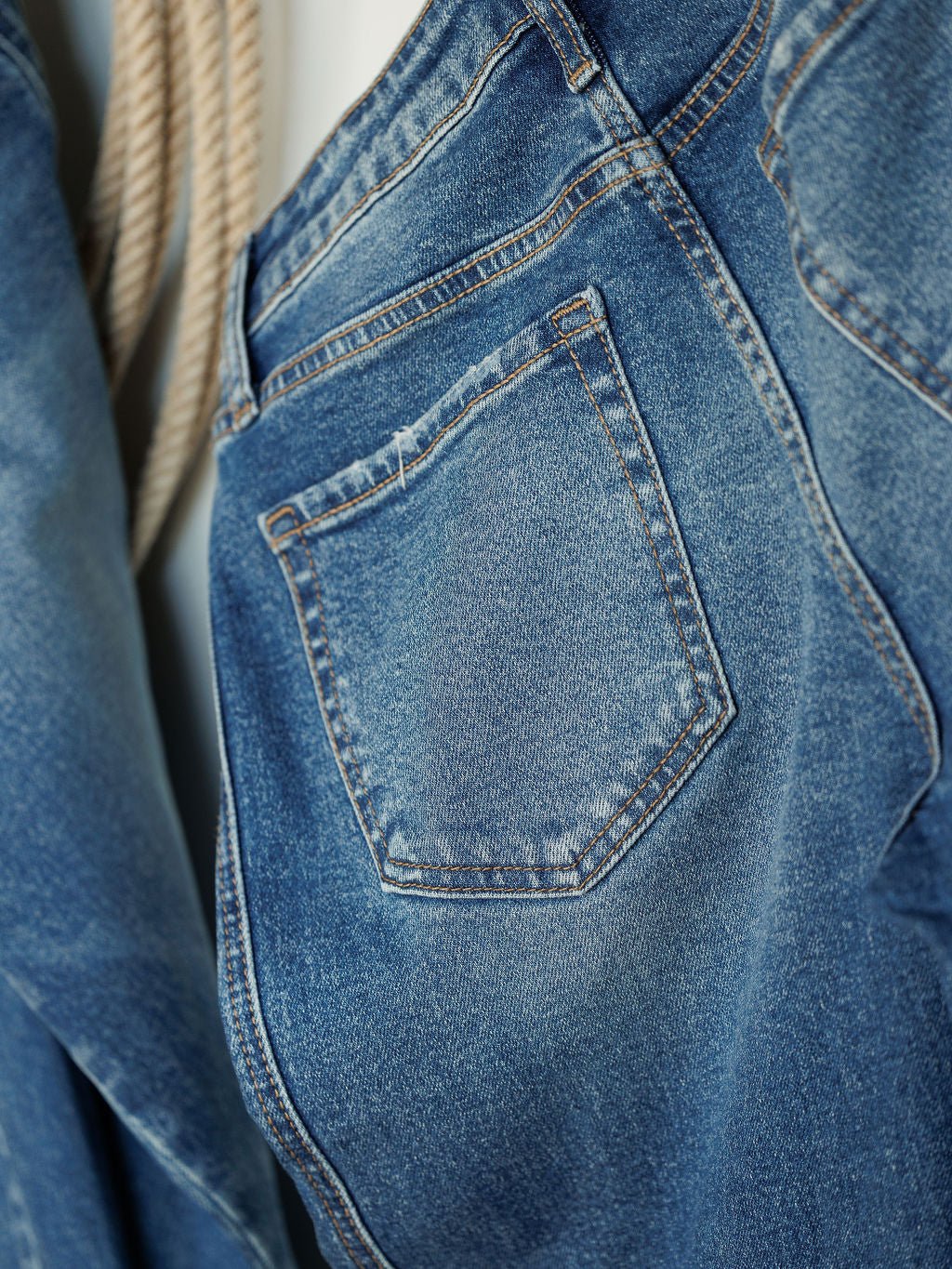 Close-up of the back pocket of The Kamden High Rise Barrel Jeans by Savannah Sevens western life{&}style, featuring detailed stitching and faded medium wash denim. Another section of these stylish barrel jeans is visible to the left.