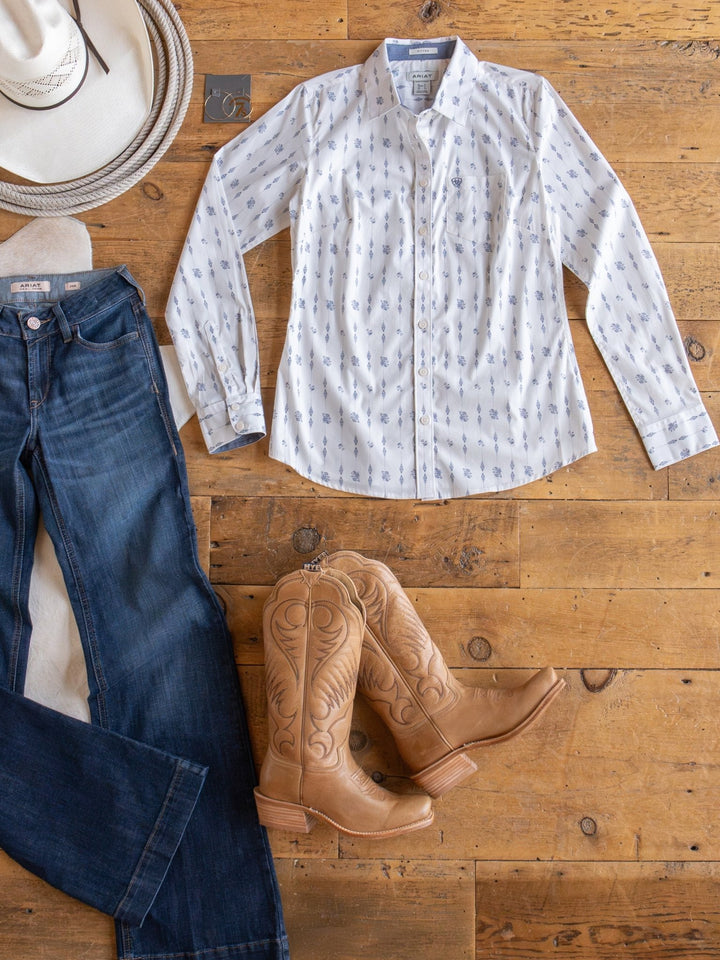 The Kearney Ariat Southwest Floral Performance Shirt from Savannah Sevens western life{&}style, paired with a cowboy hat, blue jeans, tan cowboy boots, and a coiled rope on a wooden floor creates a timeless Western-themed look.