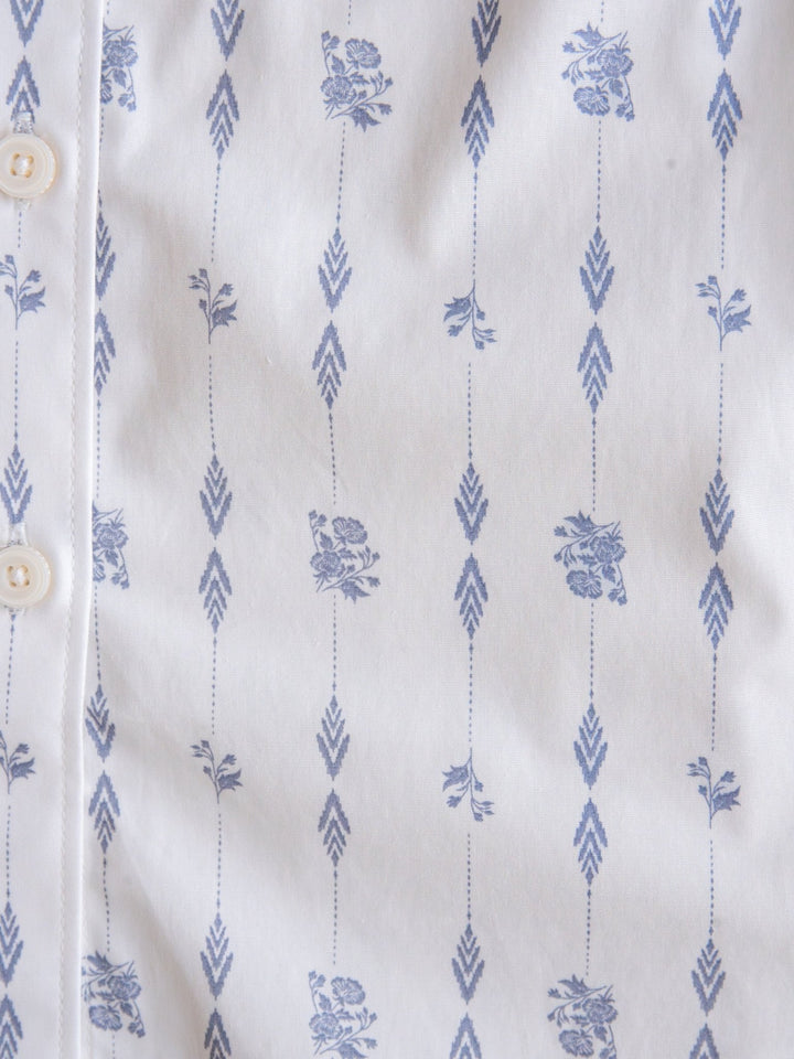 Close-up of the Kearney Ariat Southwest Floral Performance Shirt by Savannah Sevens western life{&}style in white, showcasing vertical blue arrows and small floral designs. Long sleeve button-up with white buttons is partially visible.