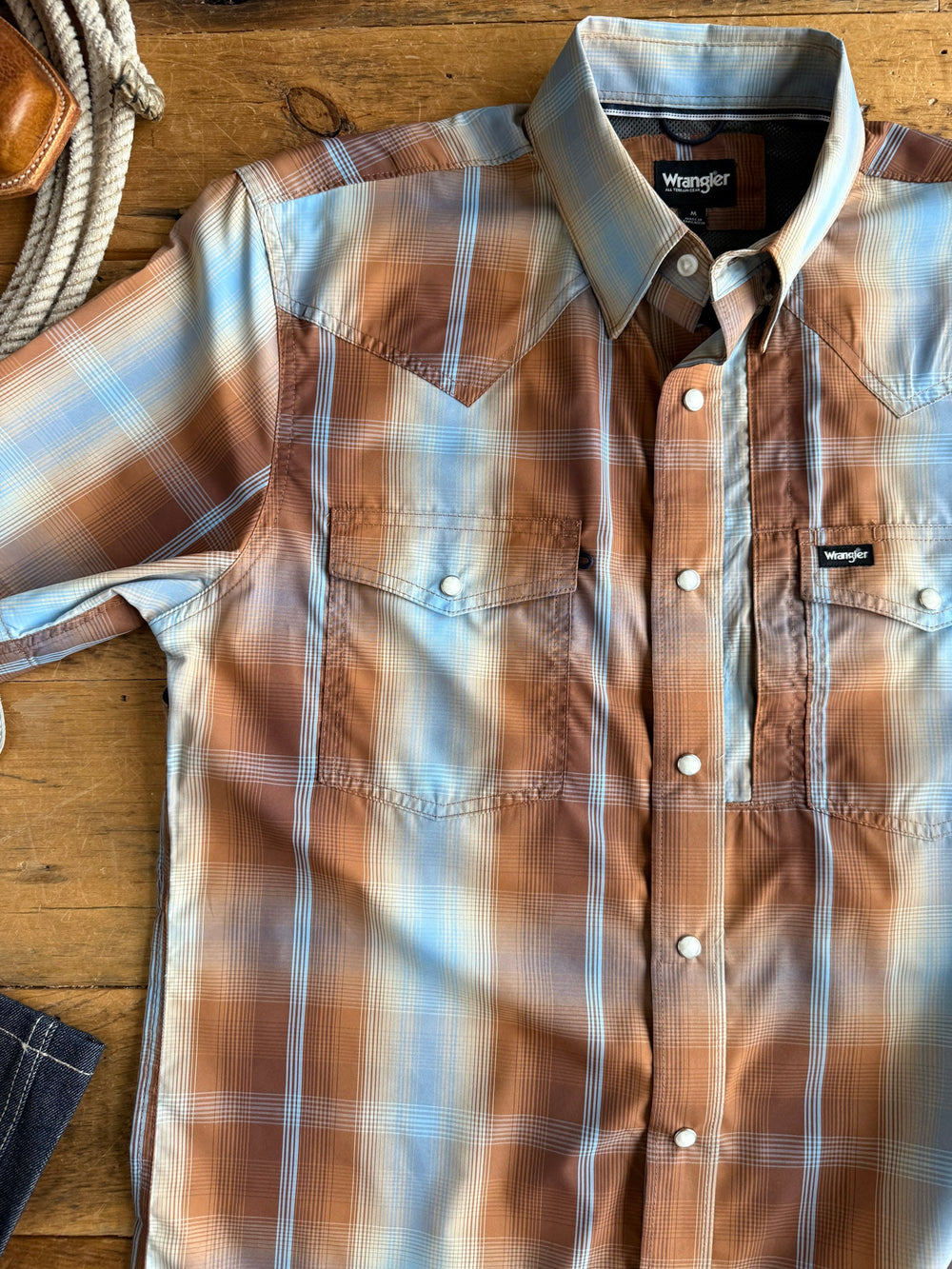 A Kent Wrangler Men's Plaid Pearl Snap shirt from Savannah Sevens western life{&}style, featuring a brown, blue, and white plaid pattern with snap buttons, is laid flat on a wooden surface. A portion of rope and denim jeans can be seen near the edges of the shirt.