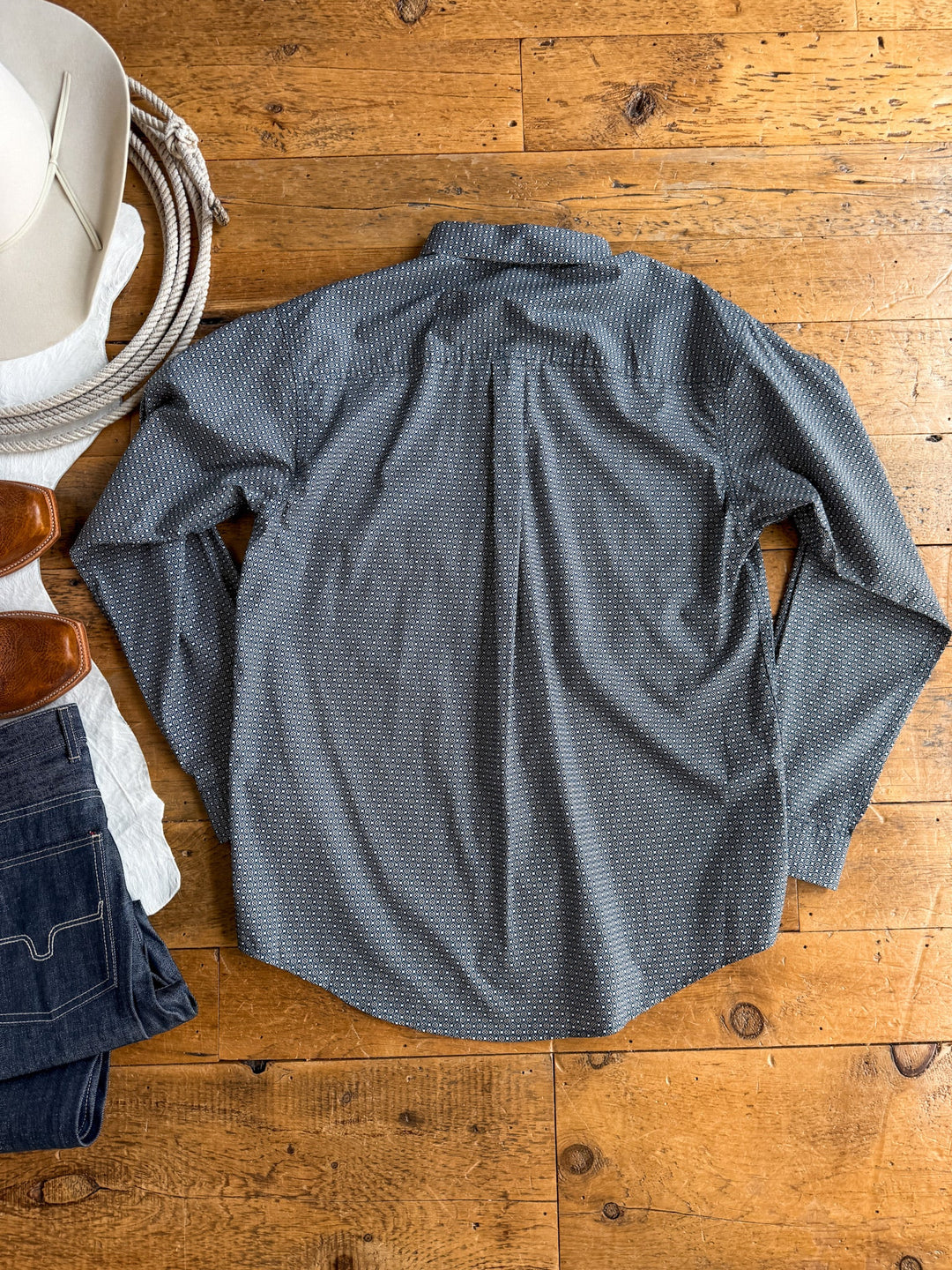 The Kenton Cinch Men’s Southwest Button Up from Savannah Sevens western life{&}style is displayed flat on a wooden floor. Arranged nearby are a pair of jeans, brown shoes, a white hat, and a partially visible rope along the left edge of the image.