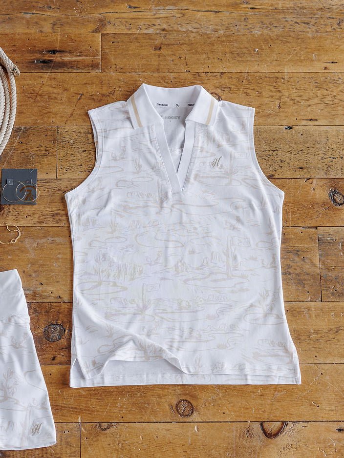 The Kerrick golf top by Savannah Sevens western life{&}style (S-XXL) in white with a subtle light beige nature pattern is displayed flat on a rustic wooden floor, with part of the matching set and a rope with tag nearby.