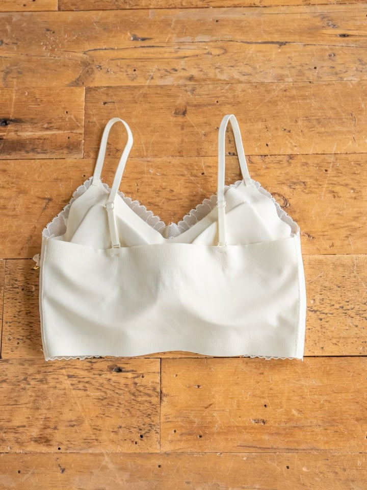 The Savannah Sevens western life{&}style Kersey Bralette, featuring white scalloped lace trim and adjustable straps, is laid flat on a wooden surface.