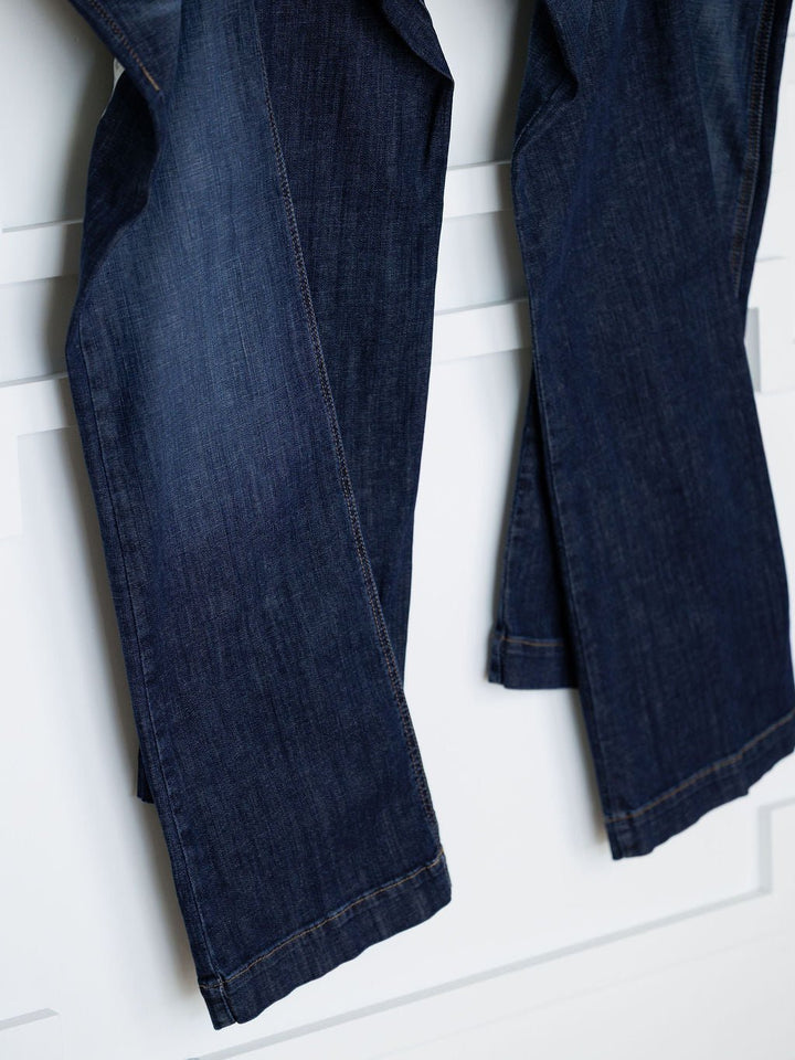 A close-up of two pairs of Ariat The Kolt Perfect Rise Trouser Jeans in a medium dark wash, showcasing their lower legs against a white background.