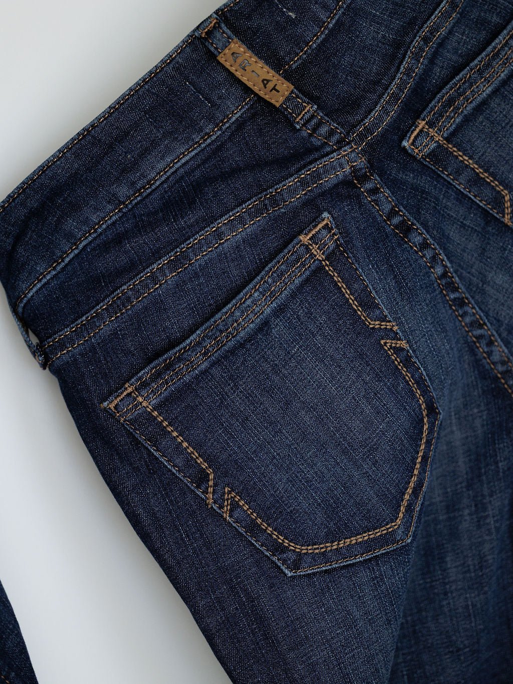 Close-up of the back pocket and waistband of Ariat’s The Kolt Perfect Rise Trouser Jean in medium dark wash, with brown stitching and a small brown label on the waistband for a flattering rise fit.