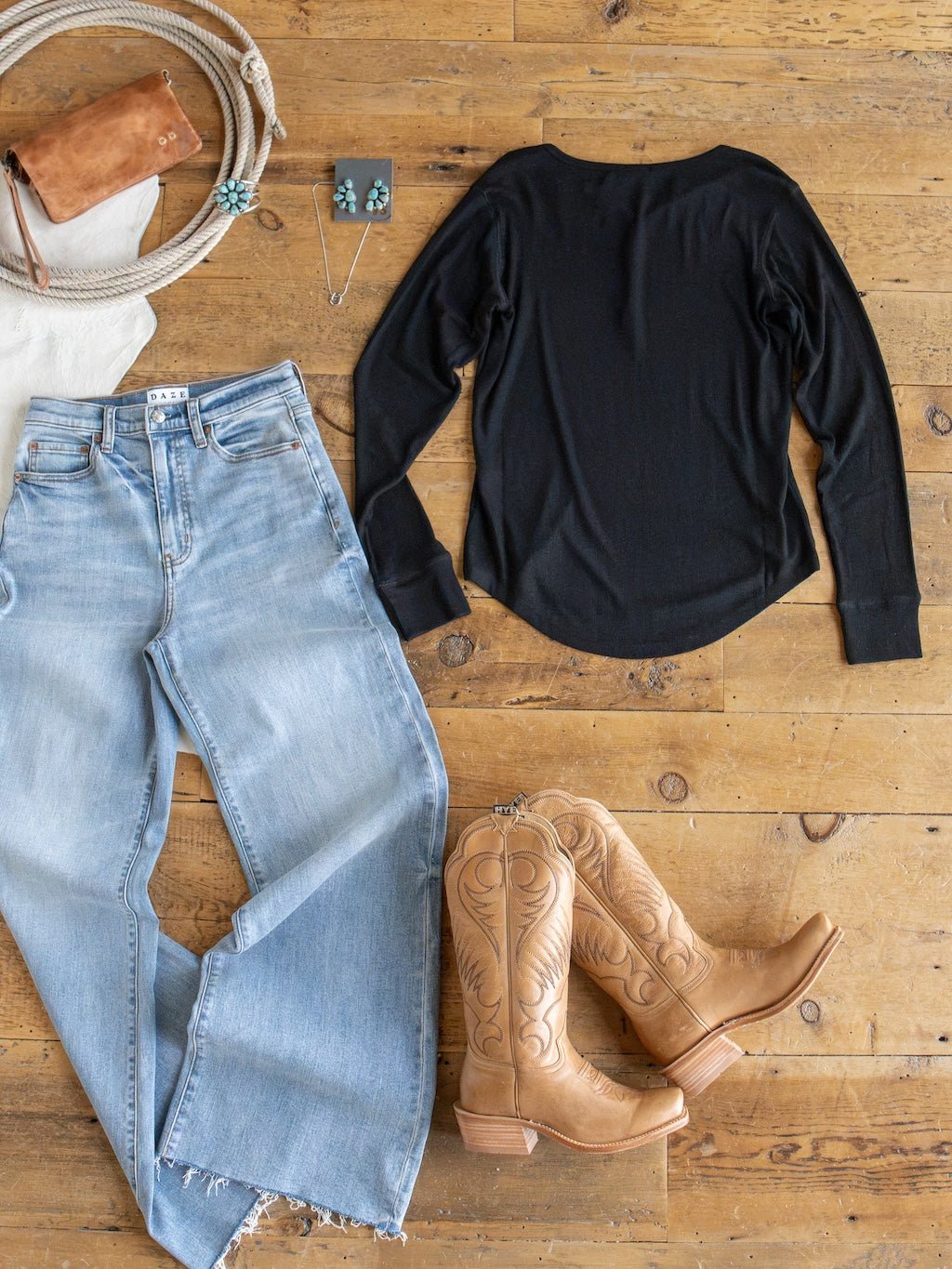 Lakota Black Ribbed Top by Savannah Sevens western life{&}style styled in a Western outfit flat lay: light blue jeans, tan cowboy boots, brown purse, coiled rope, and turquoise jewelry—all arranged on a wooden floor.
