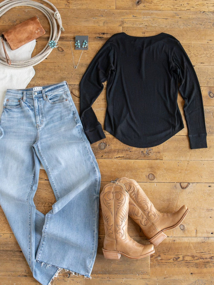Lakota Black Ribbed Top by Savannah Sevens western life{&}style styled in a Western outfit flat lay: light blue jeans, tan cowboy boots, brown purse, coiled rope, and turquoise jewelry—all arranged on a wooden floor.
