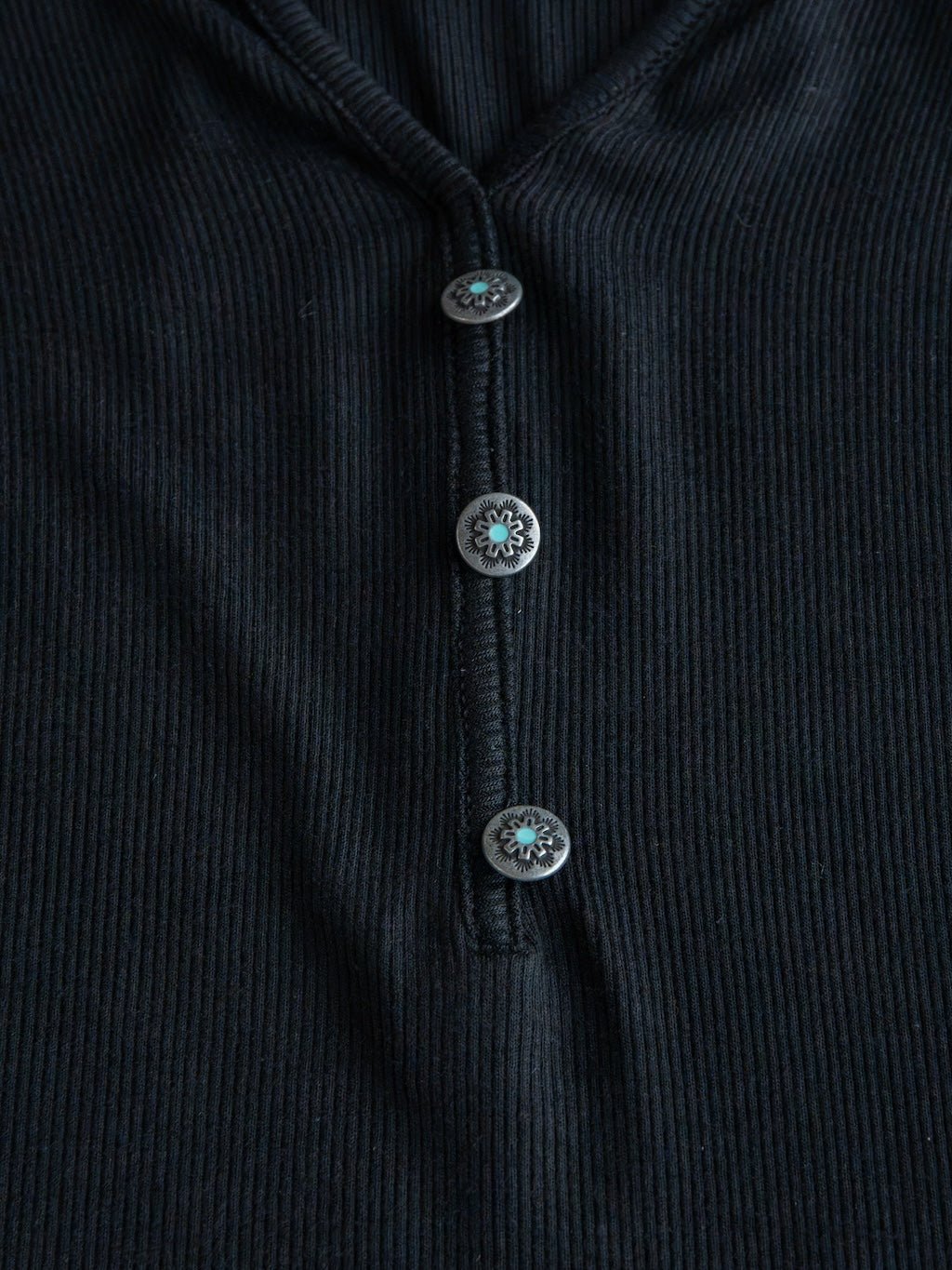 Close-up of the Lakota Black Ribbed Top by Savannah Sevens western life{&}style, showcasing its ribbed fabric and three round decorative buttons arranged vertically down the front.