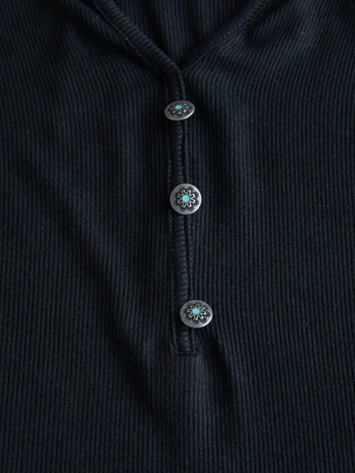Close-up of the Lakota Black Ribbed Top by Savannah Sevens western life{&}style, showcasing its ribbed fabric and three round decorative buttons arranged vertically down the front.