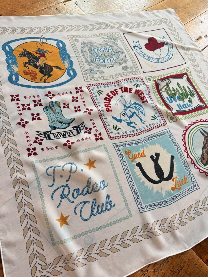 The Lamesa Neck Scarf by Savannah Sevens western life{&}style features a western graphic print with nine colorful vintage-style patches—cowboy hats, boots, horses, and phrases like T.P. Rodeo Club—displayed on a wooden floor.