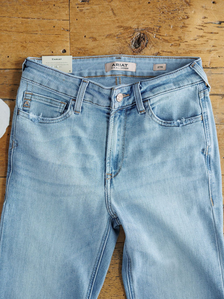The Langdon High Rise Slim Trouser Jean by Savannah Sevens western life{&}style, in light blue medium wash denim, is laid flat. The waistband displays the brand label with a size tag tucked into the left belt loop.