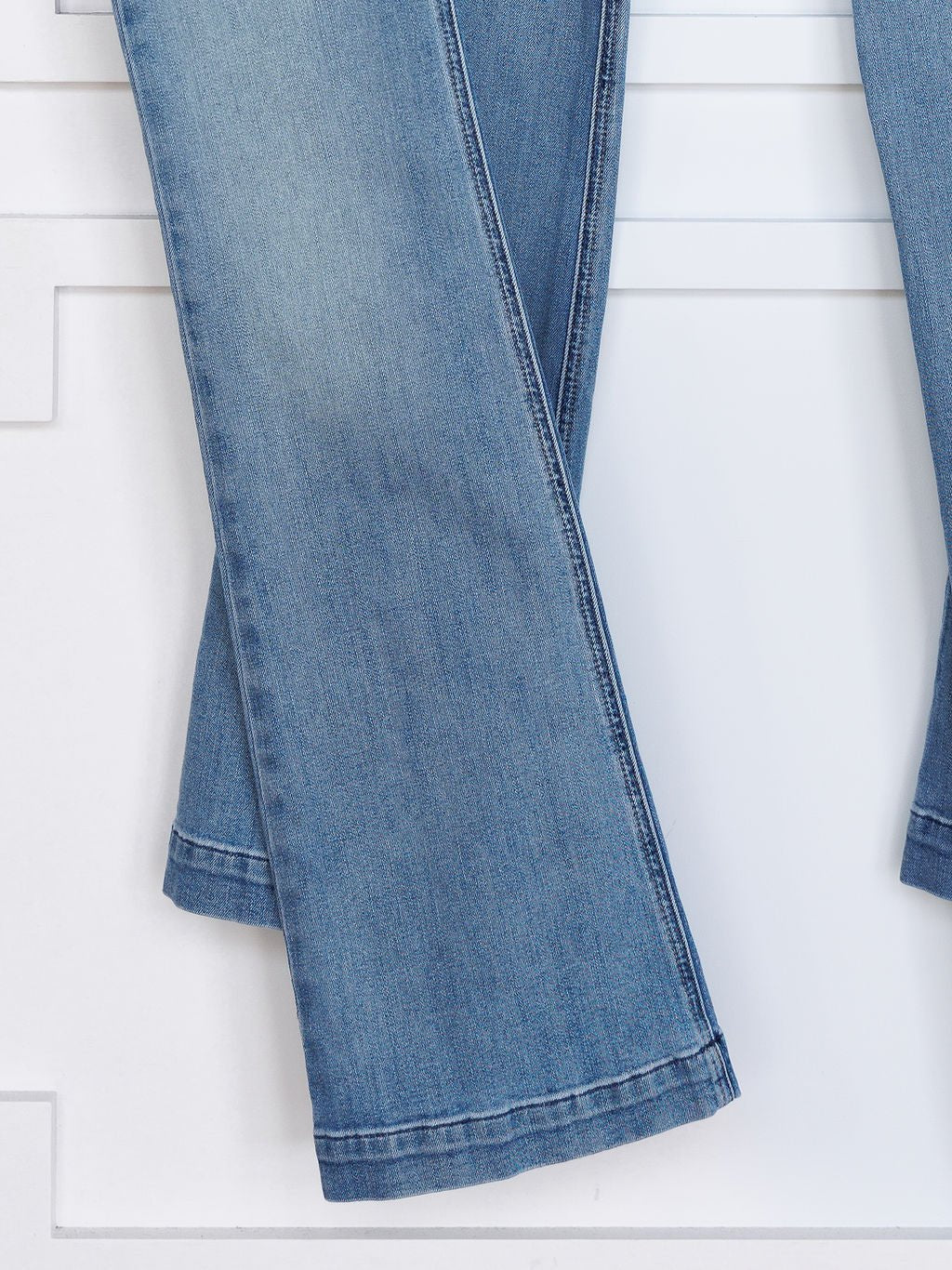 A close-up of Savannah Sevens western life{&}style's The Langdon High Rise Slim Trouser Jean in medium light wash denim with slightly flared legs, shown against a white background.
