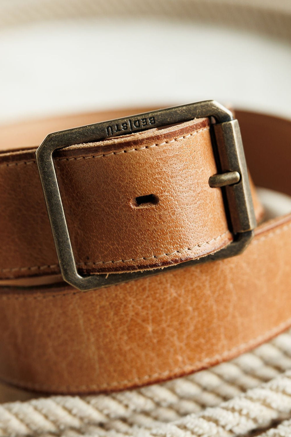 Close-up of the Langston Belt by Savannah Sevens western life{&}style, featuring tan genuine leather with fine grain and stitching, plus a rectangular metal buckle on a light textured surface.