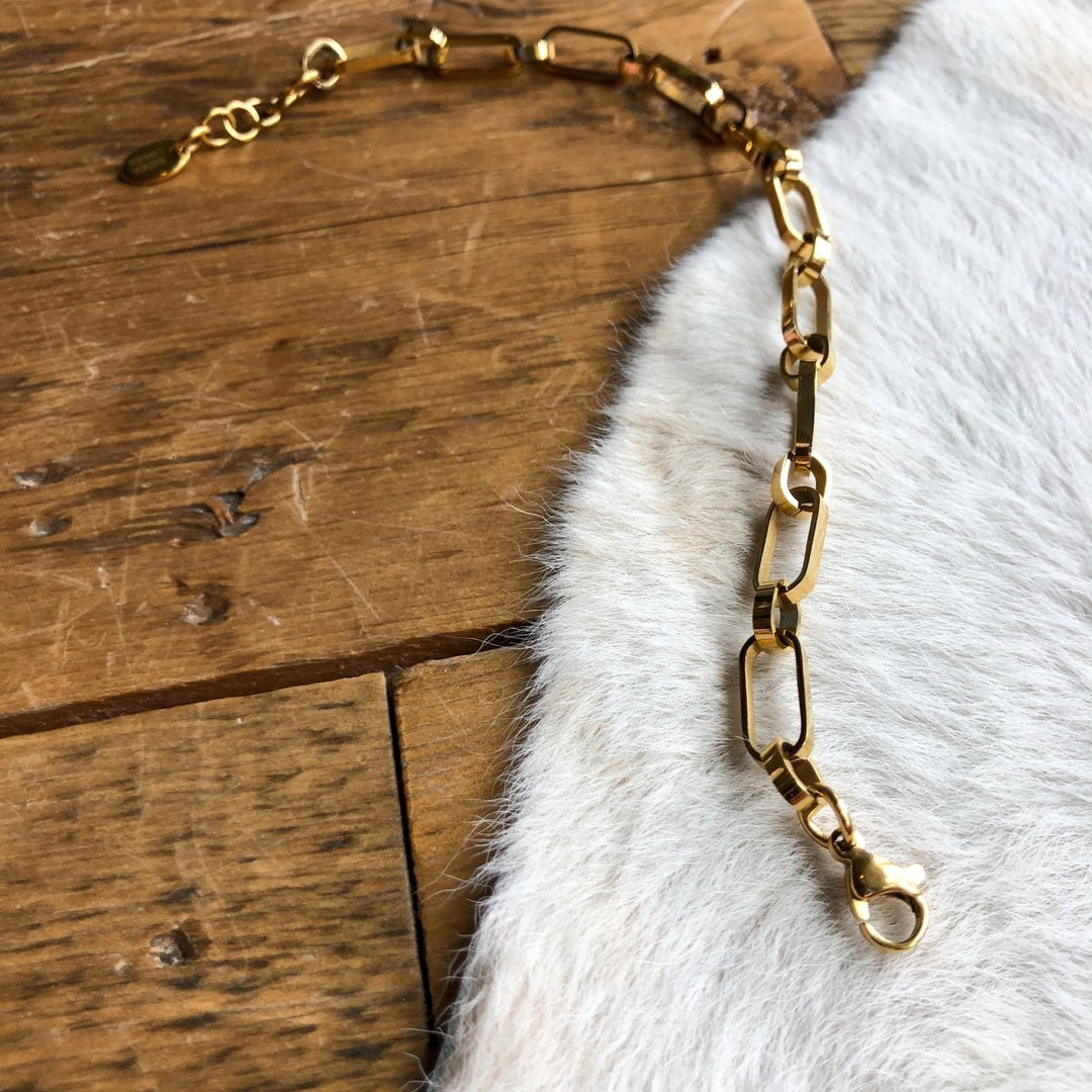The Larkin Bracelet by Savannah Sevens western life{&}style, featuring 18K gold-filled rectangular links and a lobster clasp, is displayed on white cowhide and wooden planks.