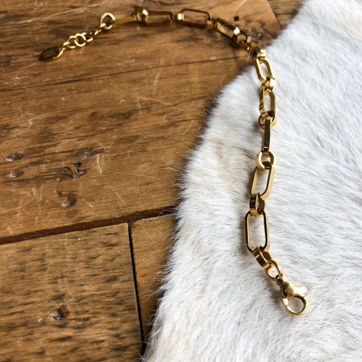 The Larkin Bracelet by Savannah Sevens western life{&}style, featuring 18K gold-filled rectangular links and a lobster clasp, is displayed on white cowhide and wooden planks.