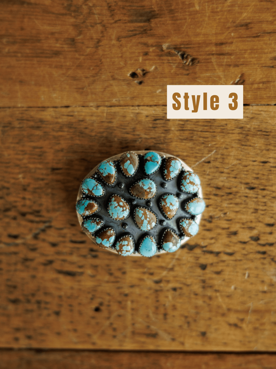 The Las Cruces Buckle by Savannah Sevens western life{&}style is displayed on a rustic wooden surface. The text Style 3 appears in a beige box in the upper right corner.