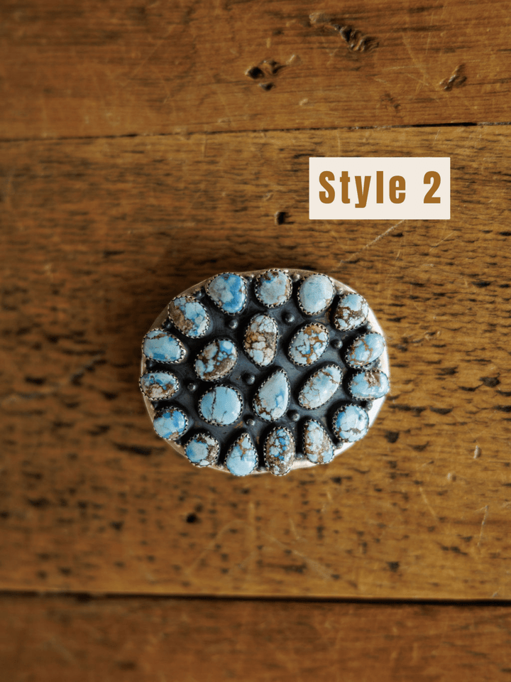 The Las Cruces Buckle by Savannah Sevens western life{&}style features multiple oval Golden HillsTurquoise stones in a cluster design, displayed on a wooden surface with "Style 2" in the upper right corner.