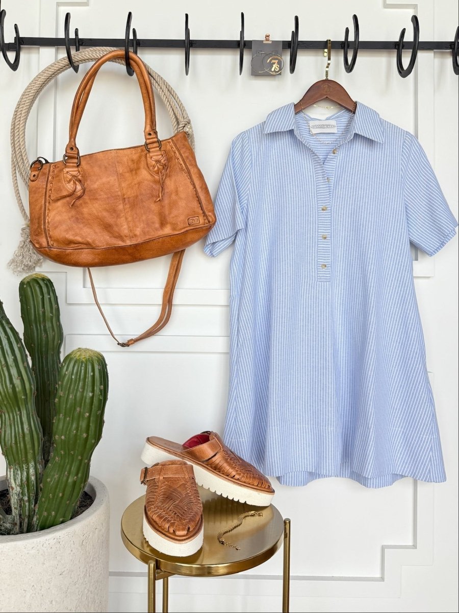 A tan leather handbag hangs beside the Leadore Blue Pinstripe Cotton Dress by Savannah Sevens western life{&}style. Below, tan woven slip-on shoes sit on a round table next to a tall green potted cactus.