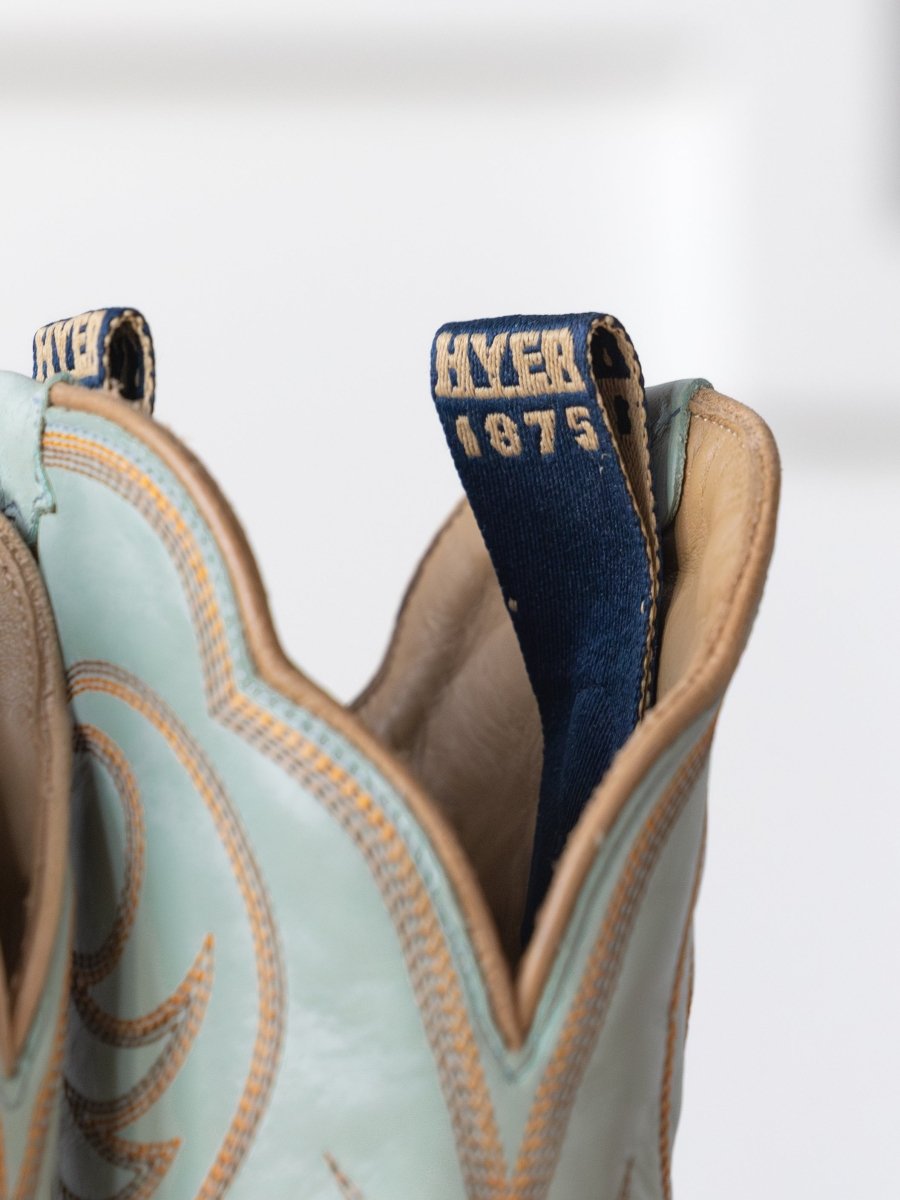 Close-up of The Hyer Leawood Boot {Robin's Egg} by Savannah Sevens western life{&}style, featuring light blue leather, tan stitching, and a navy pull tab embroidered with HYER 1875 in tan thread.