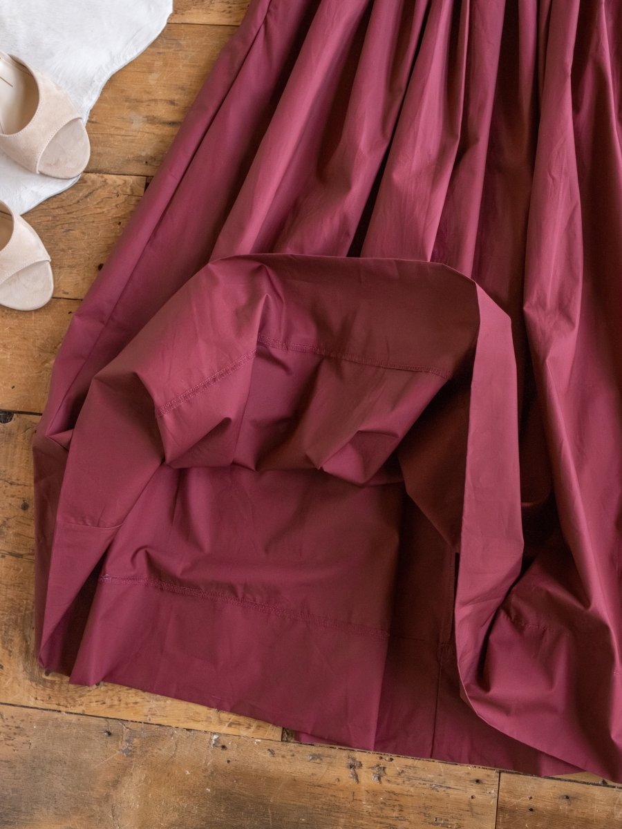 The Lenora Wine Strapless Dress by Savannah Sevens western life{&}style is spread out on a wooden floor beside a white cowhide and beige shoes.