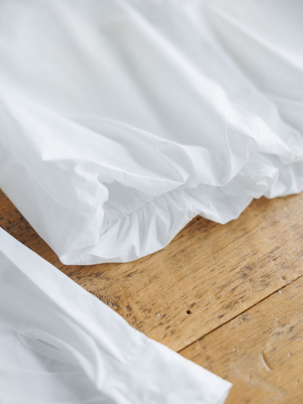 A close-up of the Levasy White Bubble Hem Cropped Button Up Top by Savannah Sevens western life{&}style, showing gathered elastic edges on clean white fabric, highlighted by natural light against a warm wooden surface.