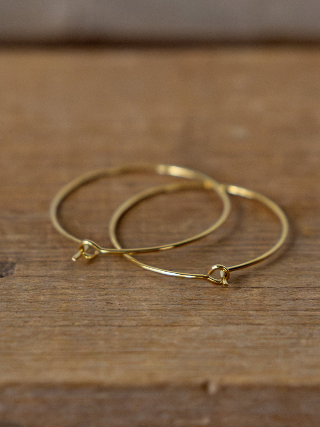 The Levy Gold/Silver Hoop Earrings by Savannah Sevens western life{&}style, known for their tarnish resistance, are displayed on a wooden surface.