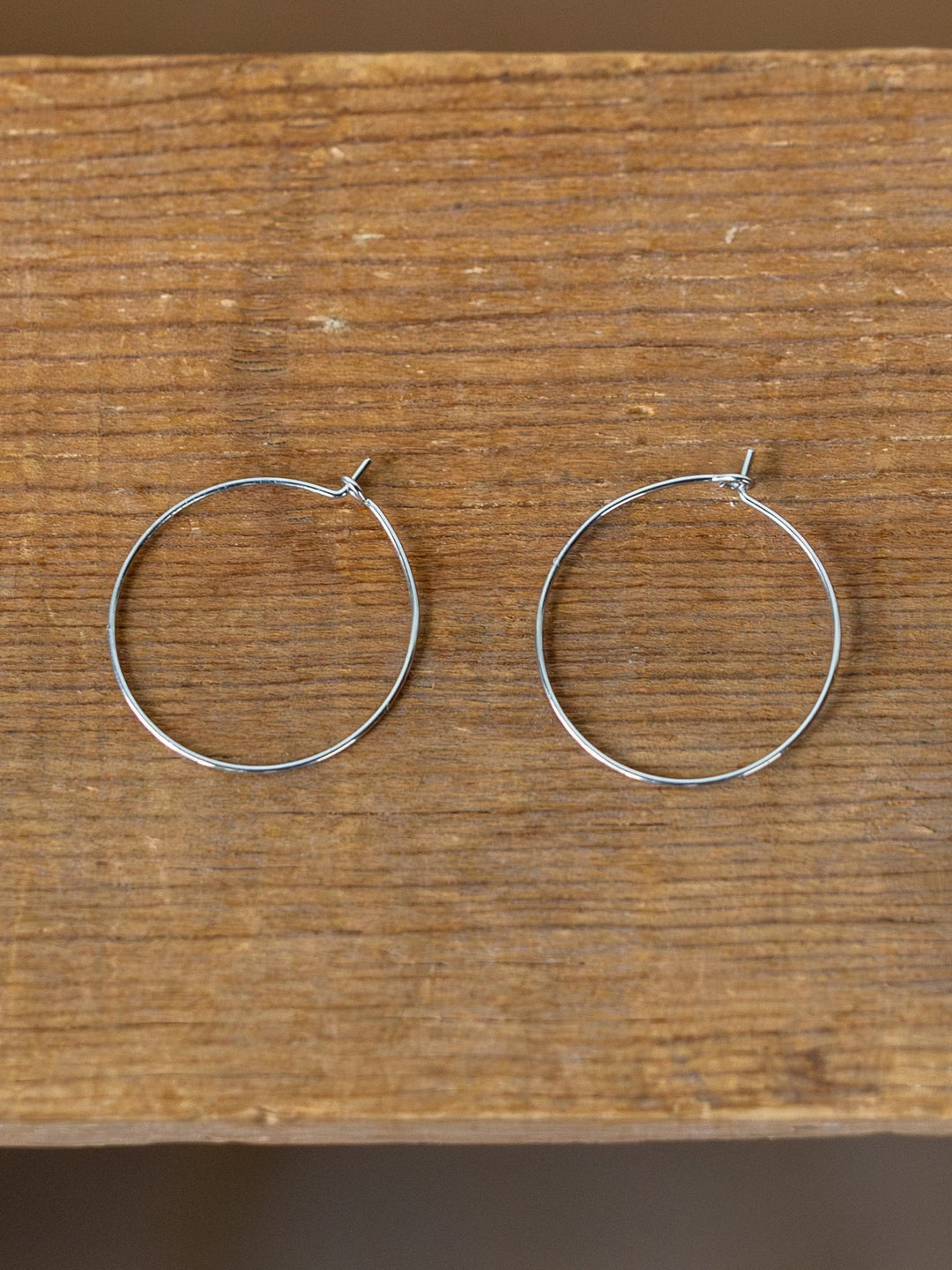 The Levy Gold/Silver Hoop Earrings by Savannah Sevens western life{&}style, known for being hypoallergenic and tarnish resistant, are displayed side by side on a wooden surface.